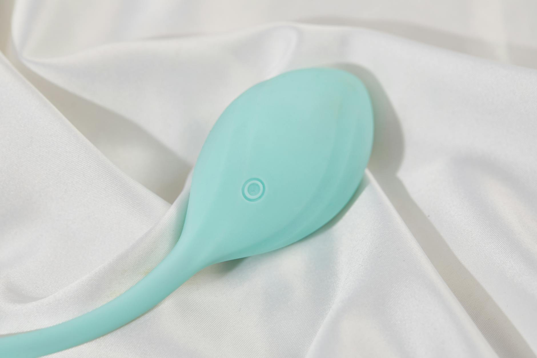 A teal clitoral vibrator on white silk, representing quality intimate wellness design