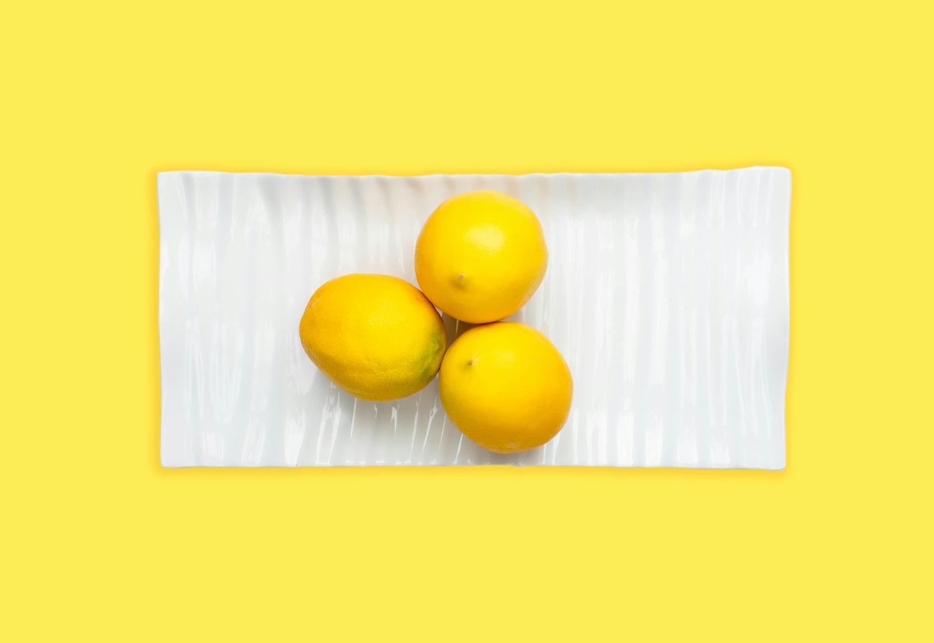 Hand holding a lemon on soft pink background, symbolizing slow, intentional pleasure