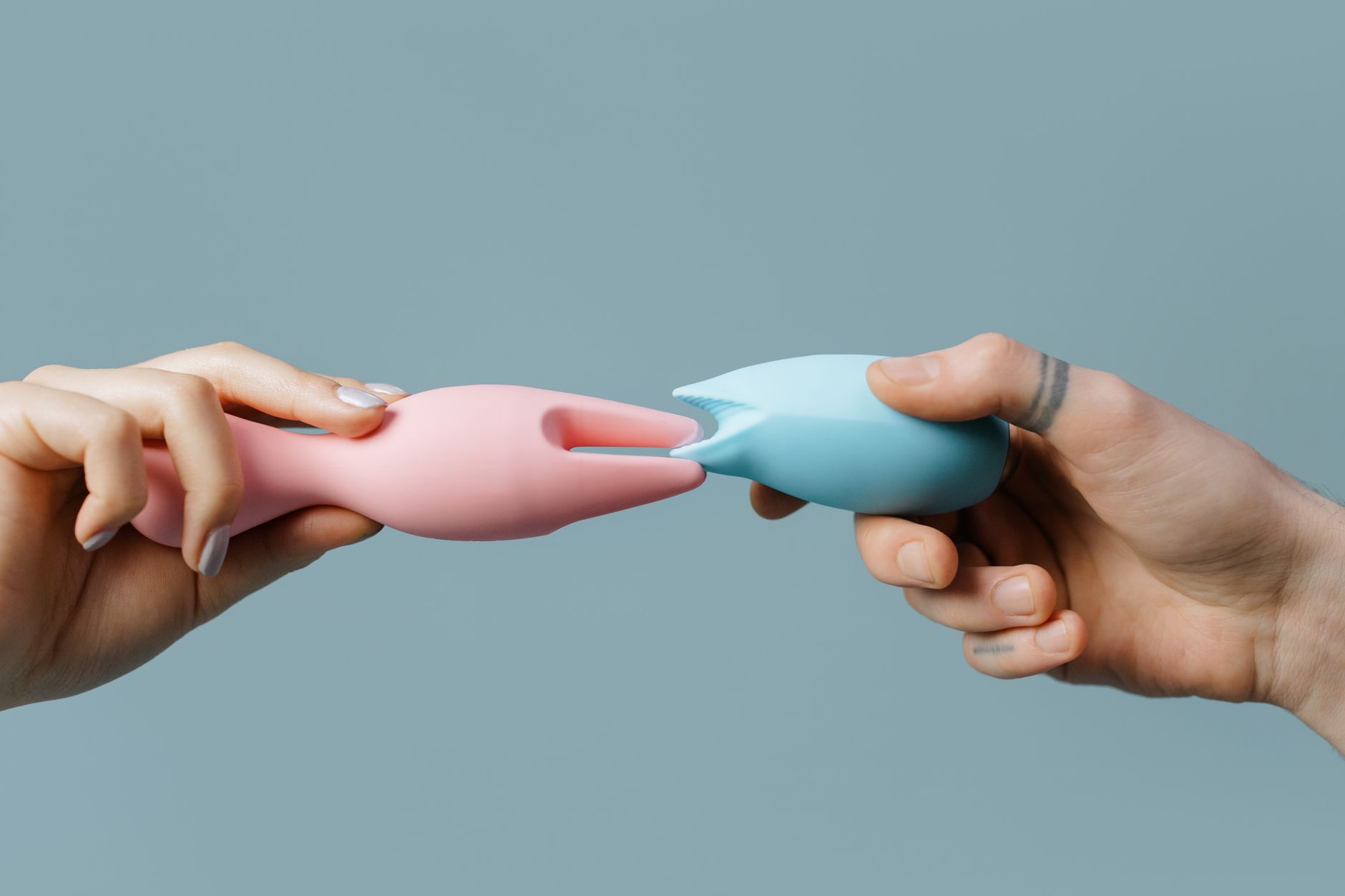 Close-up of hands holding a sleek clitoral vibrator, representing couple intimacy and shared pleasure